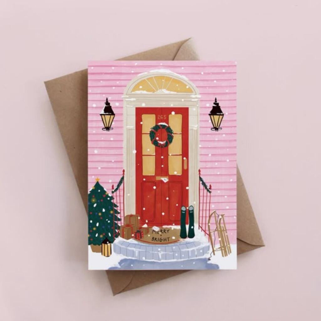 A snowy front door with boots, presents, and a doormat stating Merry and Bright