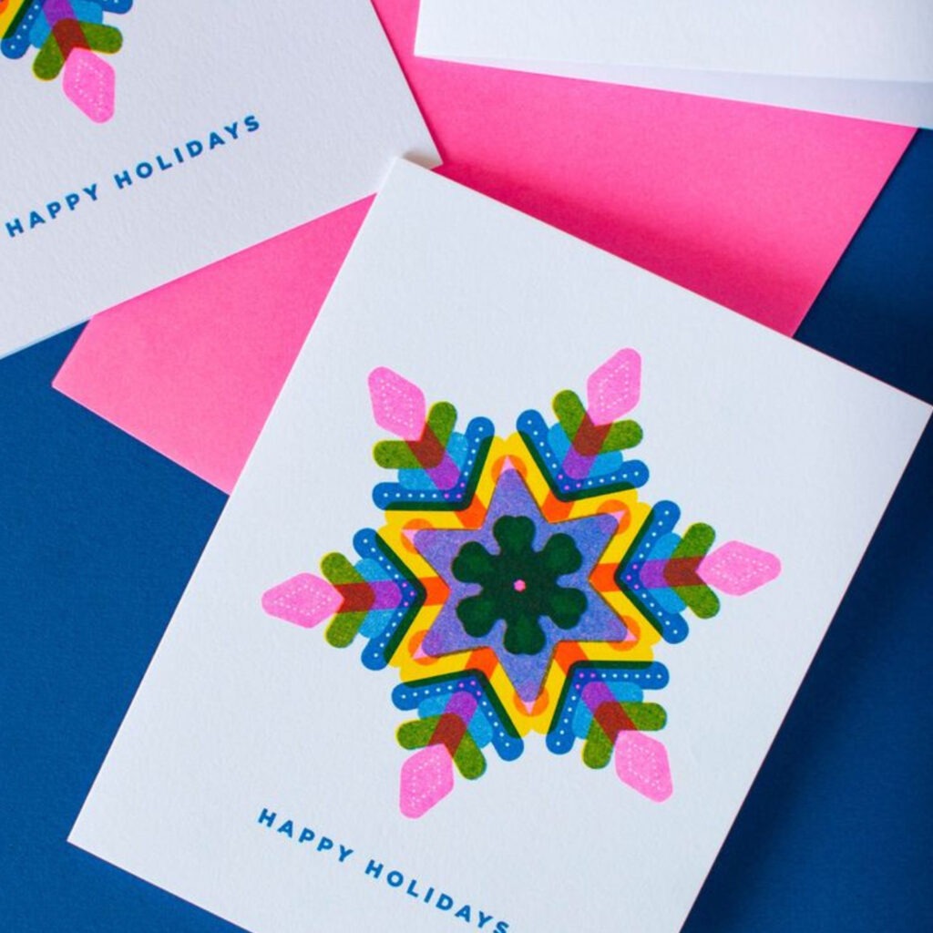 A multicoloured neon / bright snowflake, stating 'happy holidays'