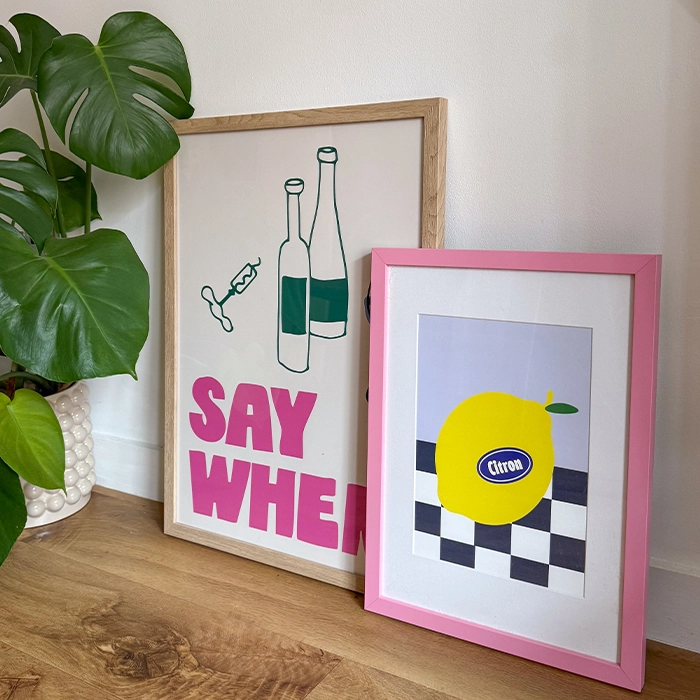 Two Framed Prints leaning against a white wall. One features an illustration of wine bottles with the caption "say when", the other features an illustration of a lemon on a black and white checkered background.
