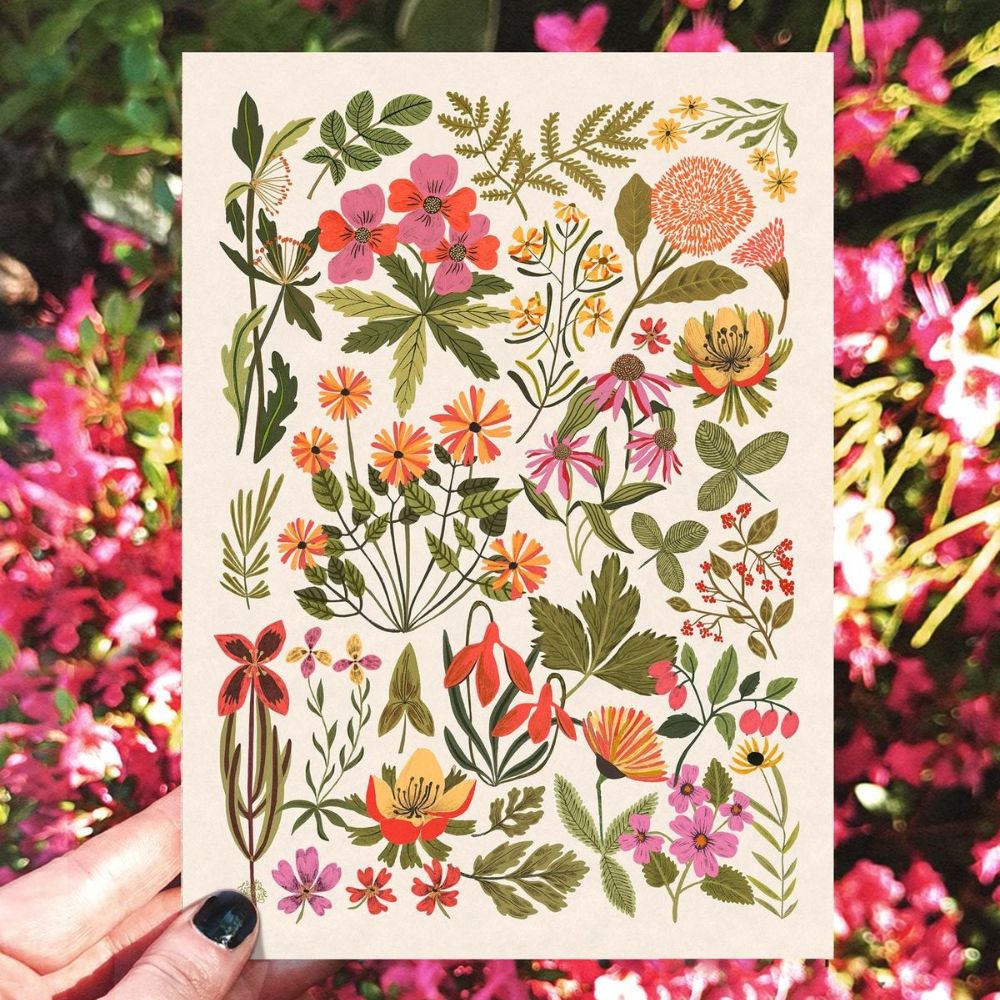 Hand holding a colourful illustrated greeting card of flowers and leaves against a floral background.