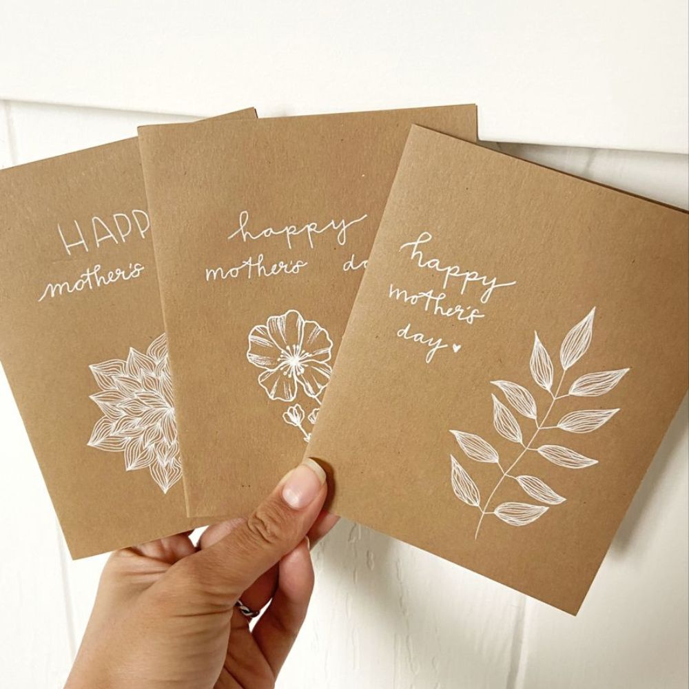 Set of three kraft paper Mother’s Day cards with white floral illustrations and handwritten-style text.