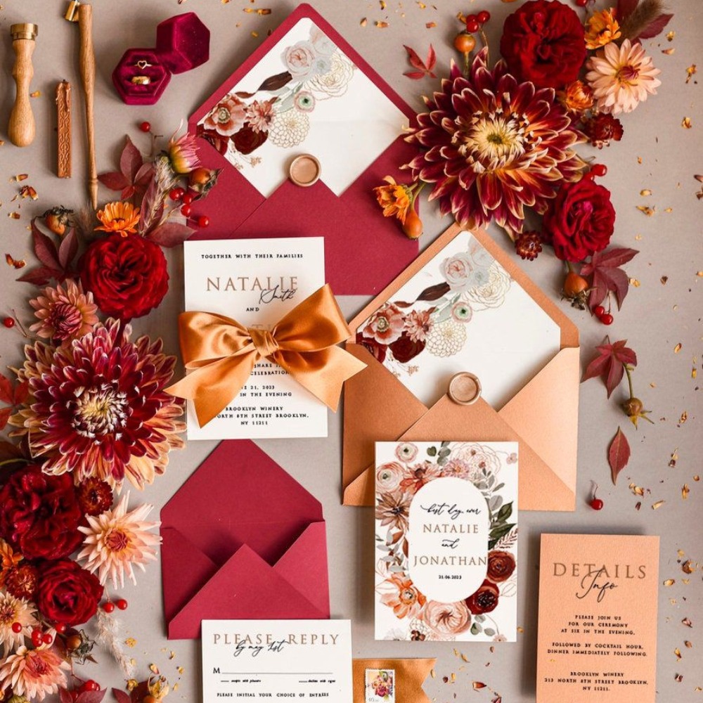 Burgundy and orange coloured wedding stationery photographed amongst similar coloured flowers. 