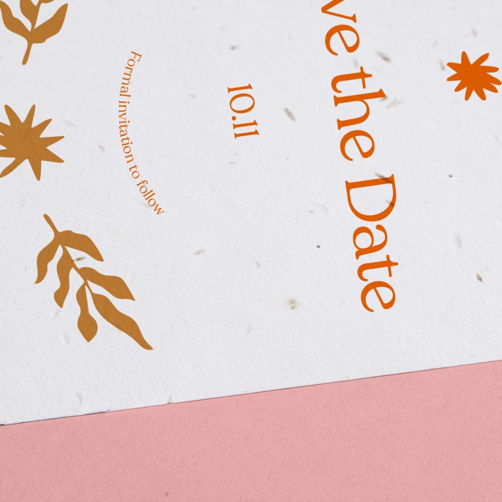 A close-up shot of a Save the Date printed on seed paper with orange wording. 