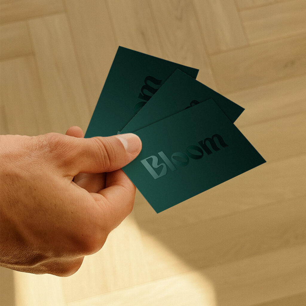 A hand holding out three forest green Business Cards with the word "Bloom" on them.