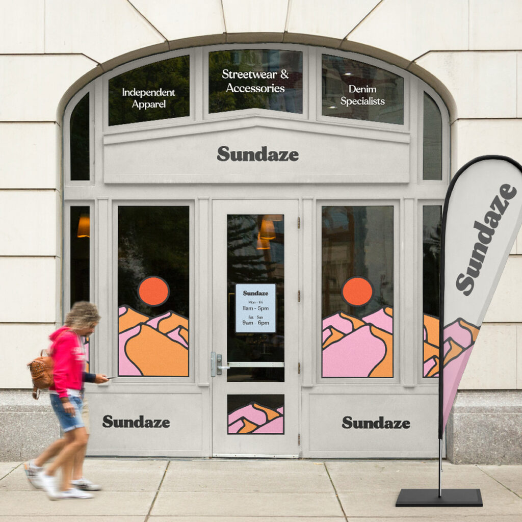 Shop front of "Sundaze" with a Flag outside and two people walking by.