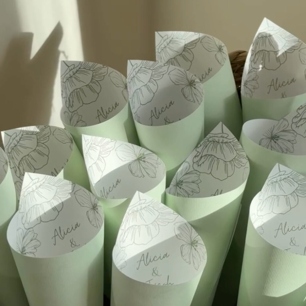 A collection of mint green paper cones arranged together, likely for wedding confetti. Each cone features a delicate line-art illustration of a flower and the personalized text "Alicia & Justin" written in an elegant script font.