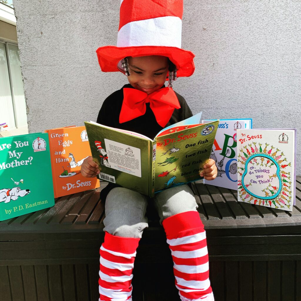 A young child dressed as "The Cat in the Hat" reading a Dr Seuss book. 