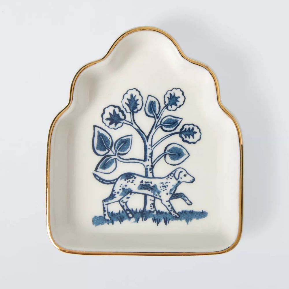 A china trinket dish with a painted design of a dog next to a tree, painted in blue. 