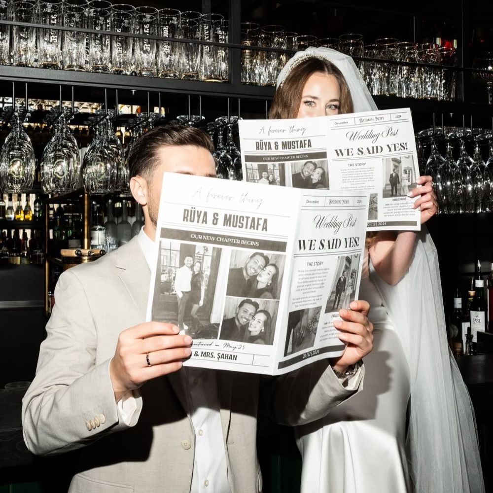 A couple in wedding attire reading their Wedding Newspaper in front of a bar. 