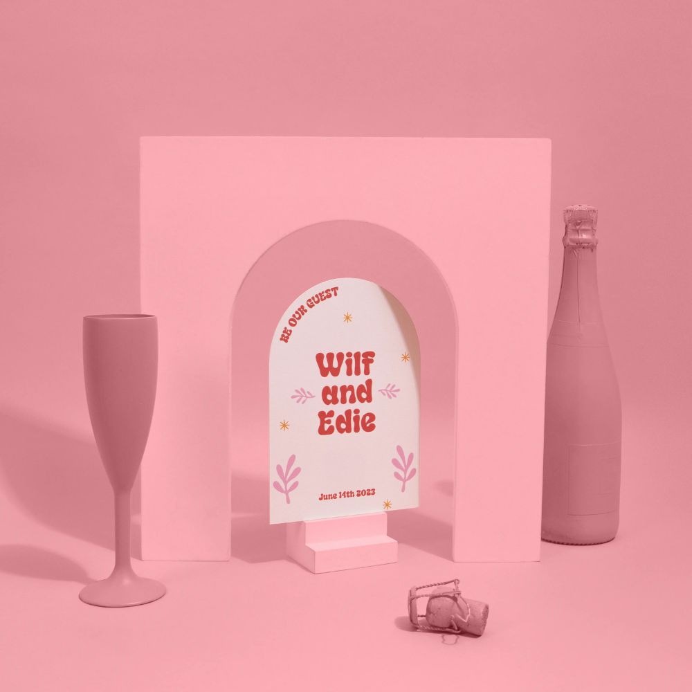 An Arch Shape Save the Date photographed on a pink background.