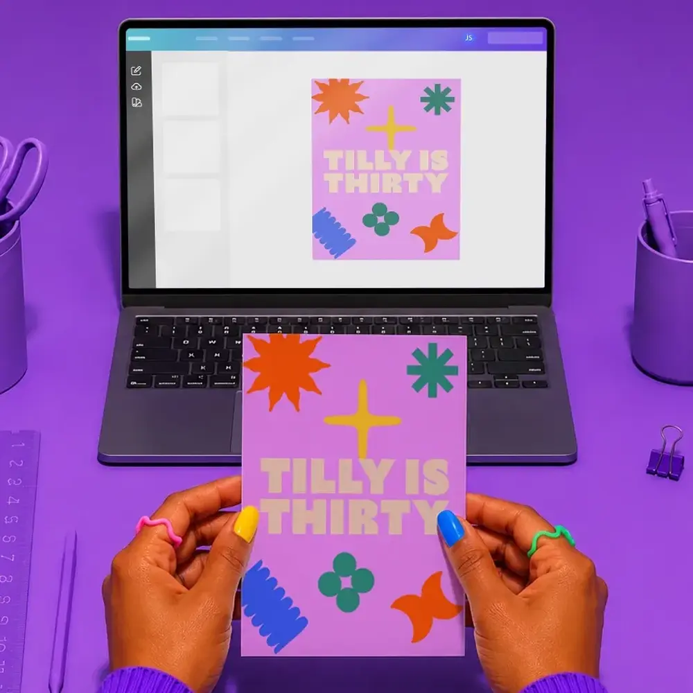 A laptop with Canva open on the screen showing a design that says "Tilly is Thirty" - in the foreground, a pair of hands hold an Invitation with the same design.