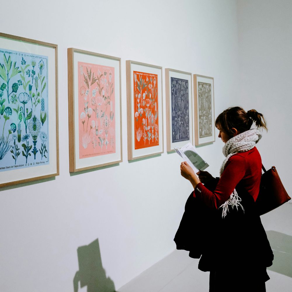 A woman reading an information booklet while standing in front of an art exhibition.