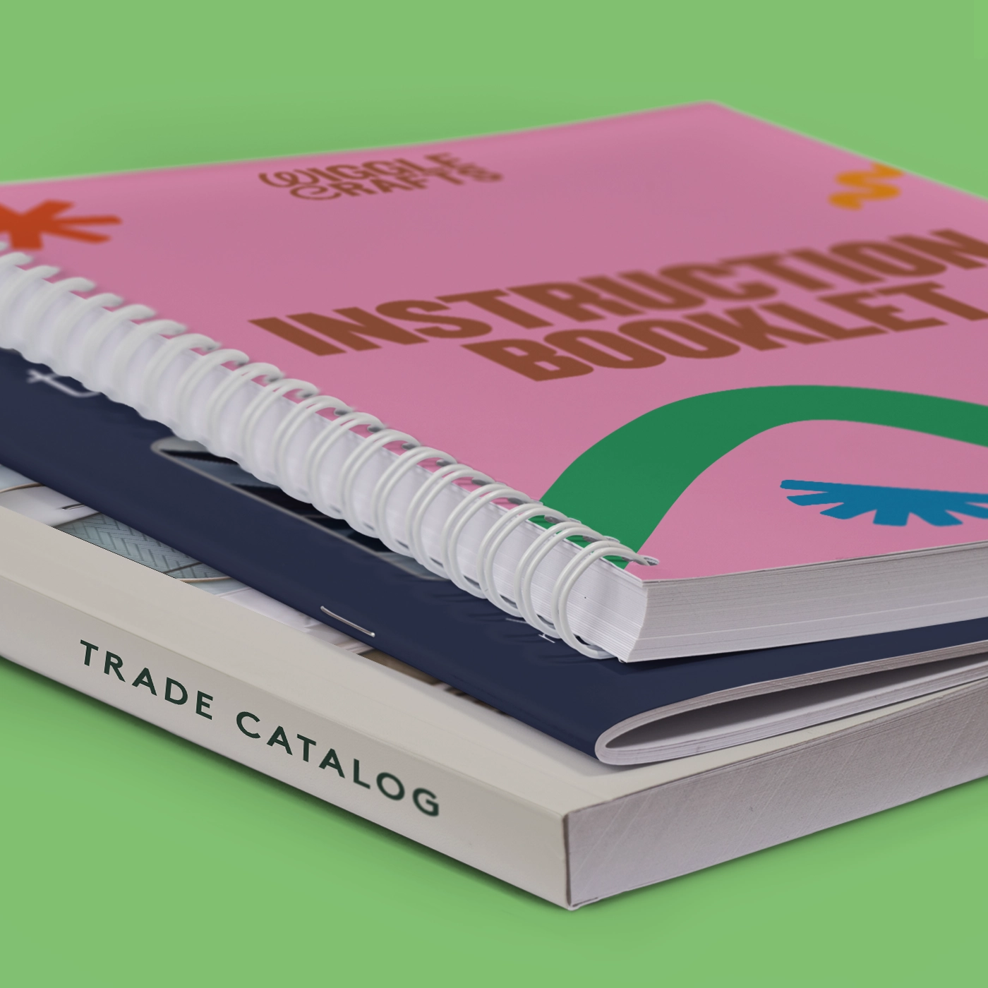Close up image of the side of several booklets with different binding types - saddle stitch, spiral bound, and perfect bound. Laid on a green background.