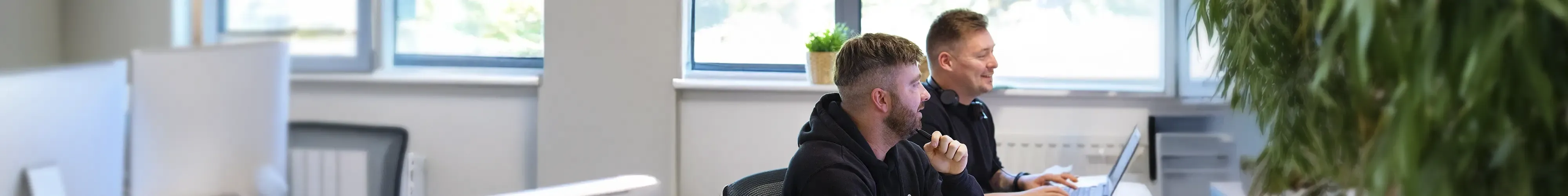Photograph of two smiling customer service team members sitting at a desk in an office environment.