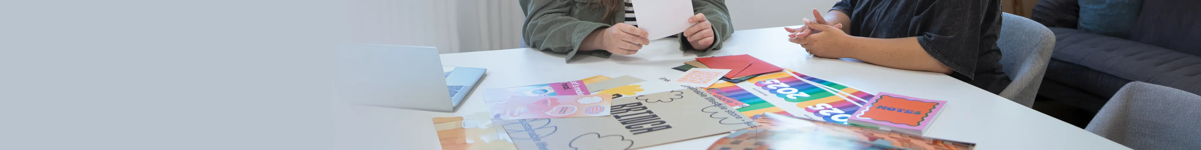 Two people sitting at a desk in an office environment surrounded by various prints with bold colorful designs.