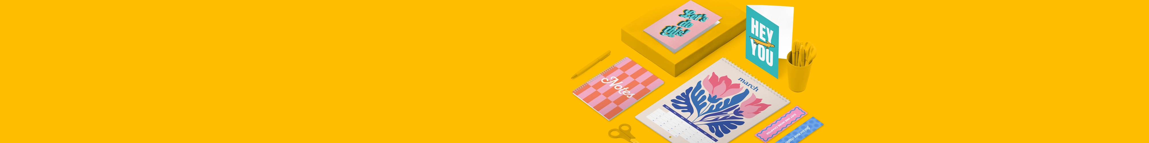 A selection of print products including greeting cards, a calendar, bookmarks and a notebook with pink, organge and blue colorful designs, laid on a yellow background featuring scissors and pencils.