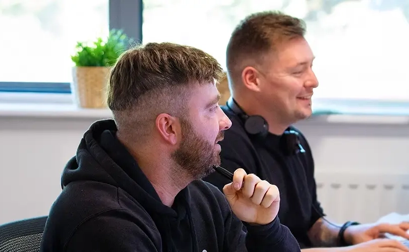 Photograph of two smiling customer service team members sitting at a desk in an office environment.