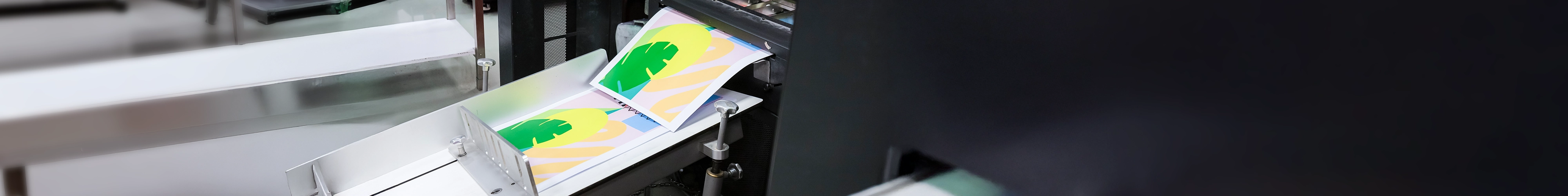 A close-up of a commercial printer producing colorful sheets featuring a bold abstract design with green, yellow, and peach shapes on a pastel background.