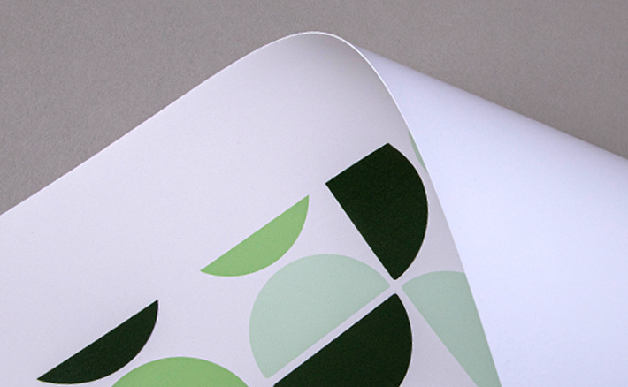 Close-up image of a single sheet of curved paper with a green abstract print on a grey background.