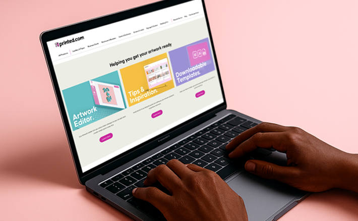A persons typing on a laptop, on a soft pink background.