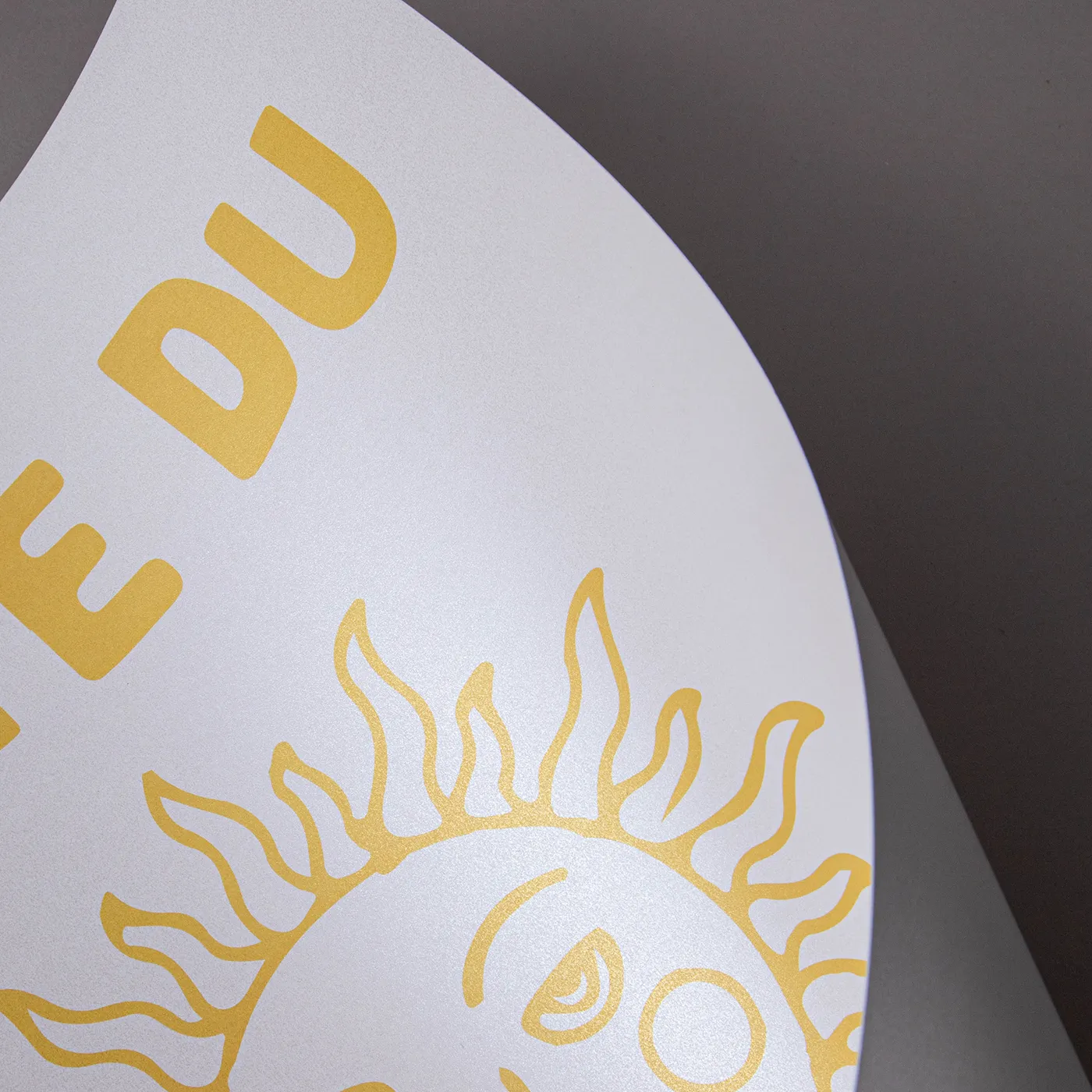 Close up image of Pearlescent paper printed with a minimal yellow sun design and positioned in a curve, demonstrating the shine.