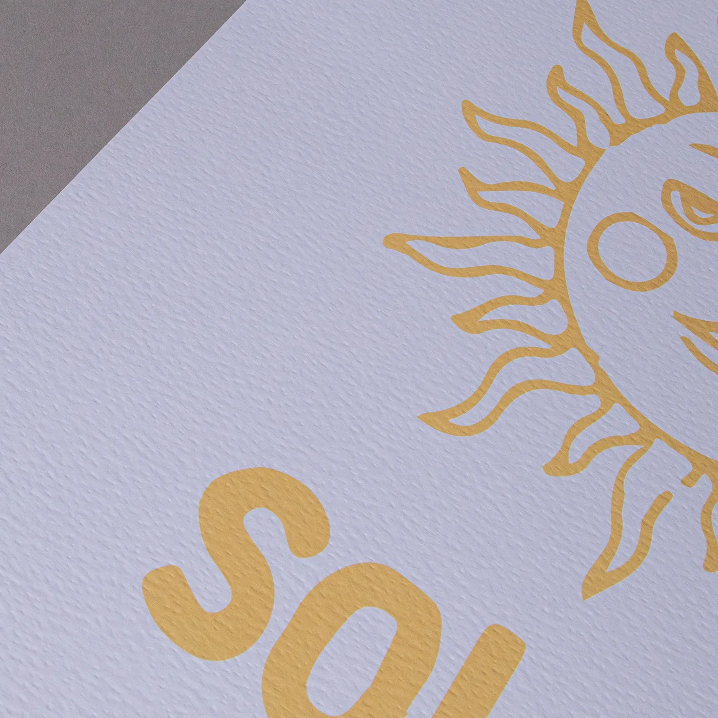 Close up of a white textured paper with a minimalist yellow sun design on a plain grey background.