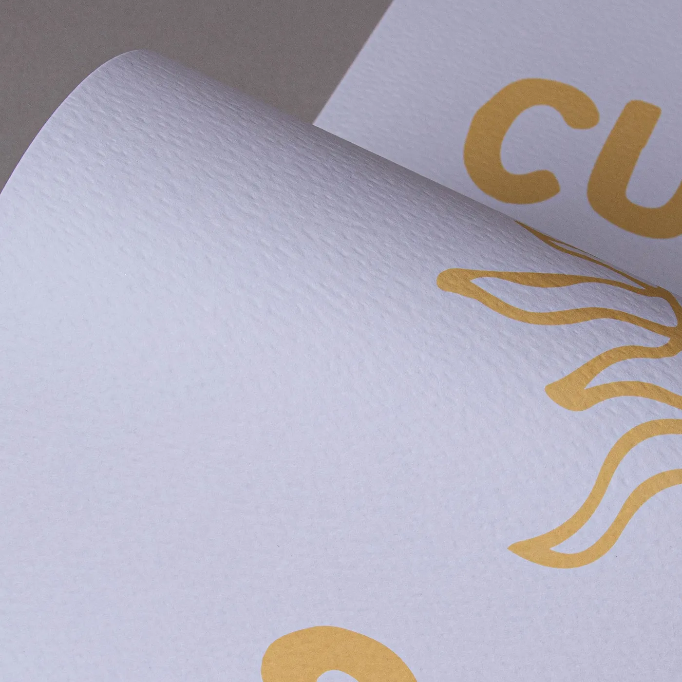 Close up of a white textured paper with a minimalist yellow sun design on a plain grey background.