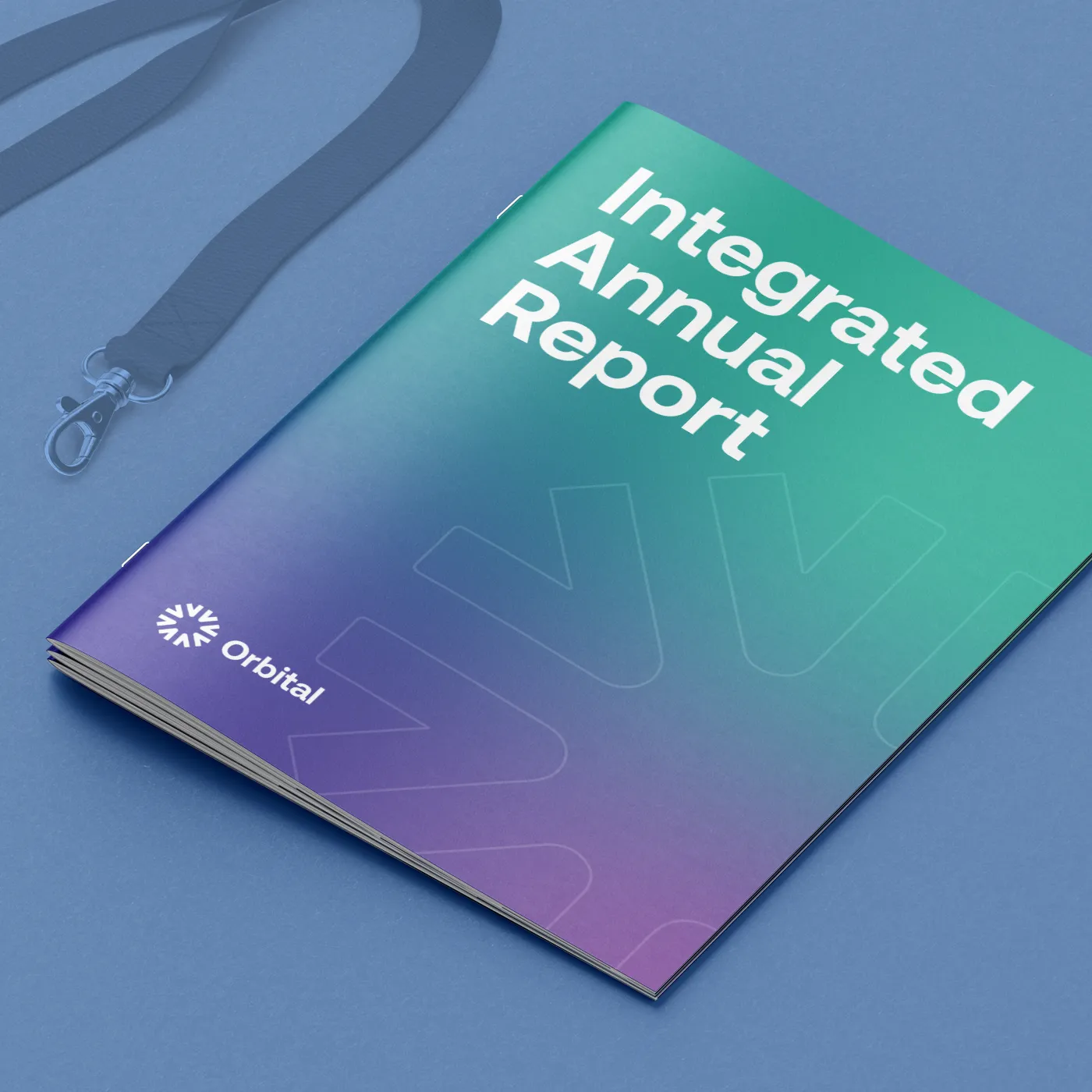 Gemini said A close-up shot of an "Integrated Annual Report" booklet by Orbital with a teal-to-purple gradient cover, positioned on a blue surface next to a blue lanyard.