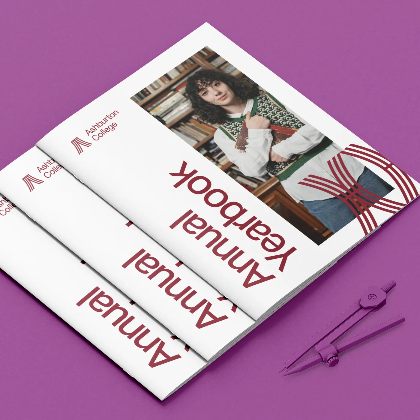 A stack of three "Annual Yearbook" booklets for Ashburton College lies on a vibrant purple surface next to a matching purple geometry compass.