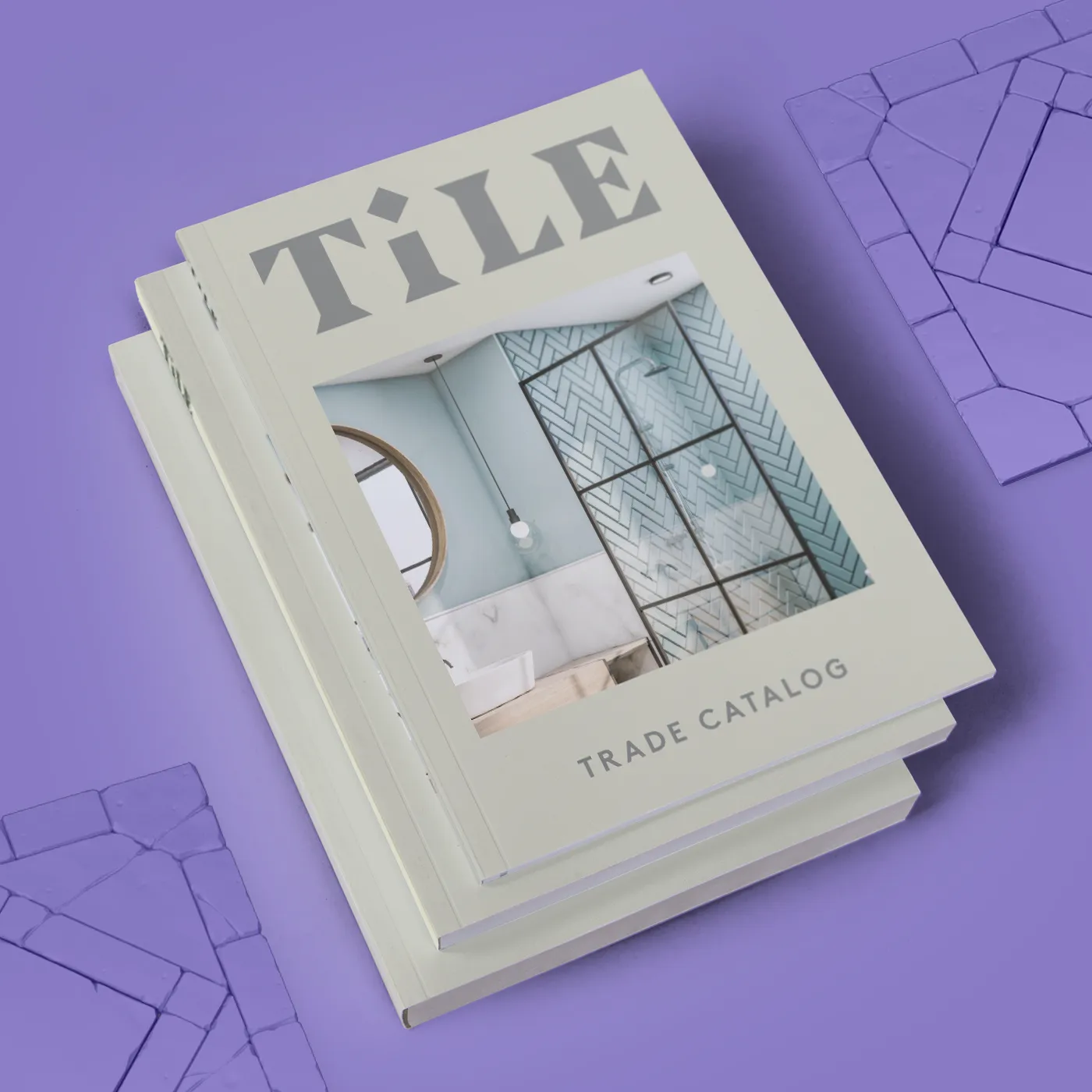 A stack of Trade Perfect Bound Catalogs titled “TILE" featuring a cover photo of a modern bathroom with light blue tiles, a round mirror, and a white sink. Subtle geometric tile patterns appear in the background.