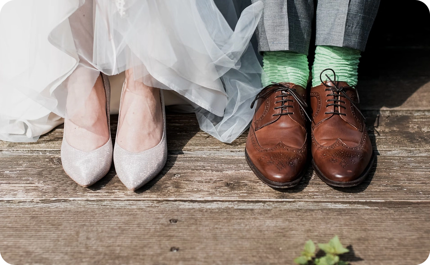 Close-up of a bride and groom's wedding footwear. Features sparkling silver bridal heels and classic brown leather oxfords paired with fun, colorful green socks, showcasing a modern and personalized wedding style.