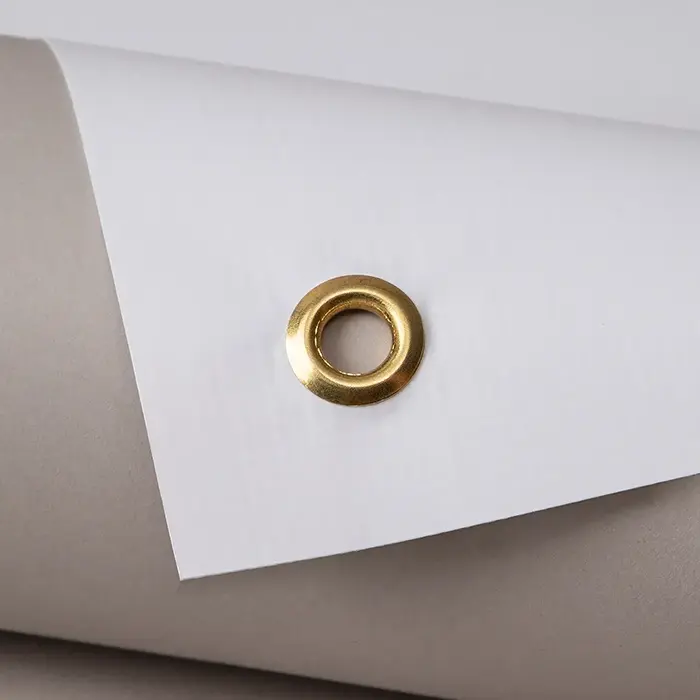A close-up shot of a single round, metallic gold eyelet embedded near the corner of a thick white sheet of material.