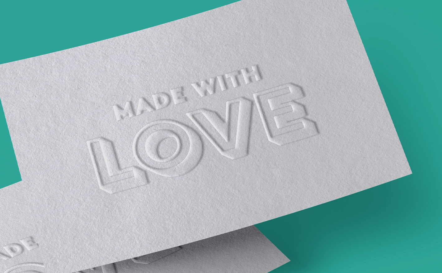 A close-up shot of a textured, off-white card showing a blind debossed or embossed finish. The text "MADE WITH LOVE" is stamped directly into the thick paper stock in a blocky 3D font style, creating a deep tactile effect without any ink.