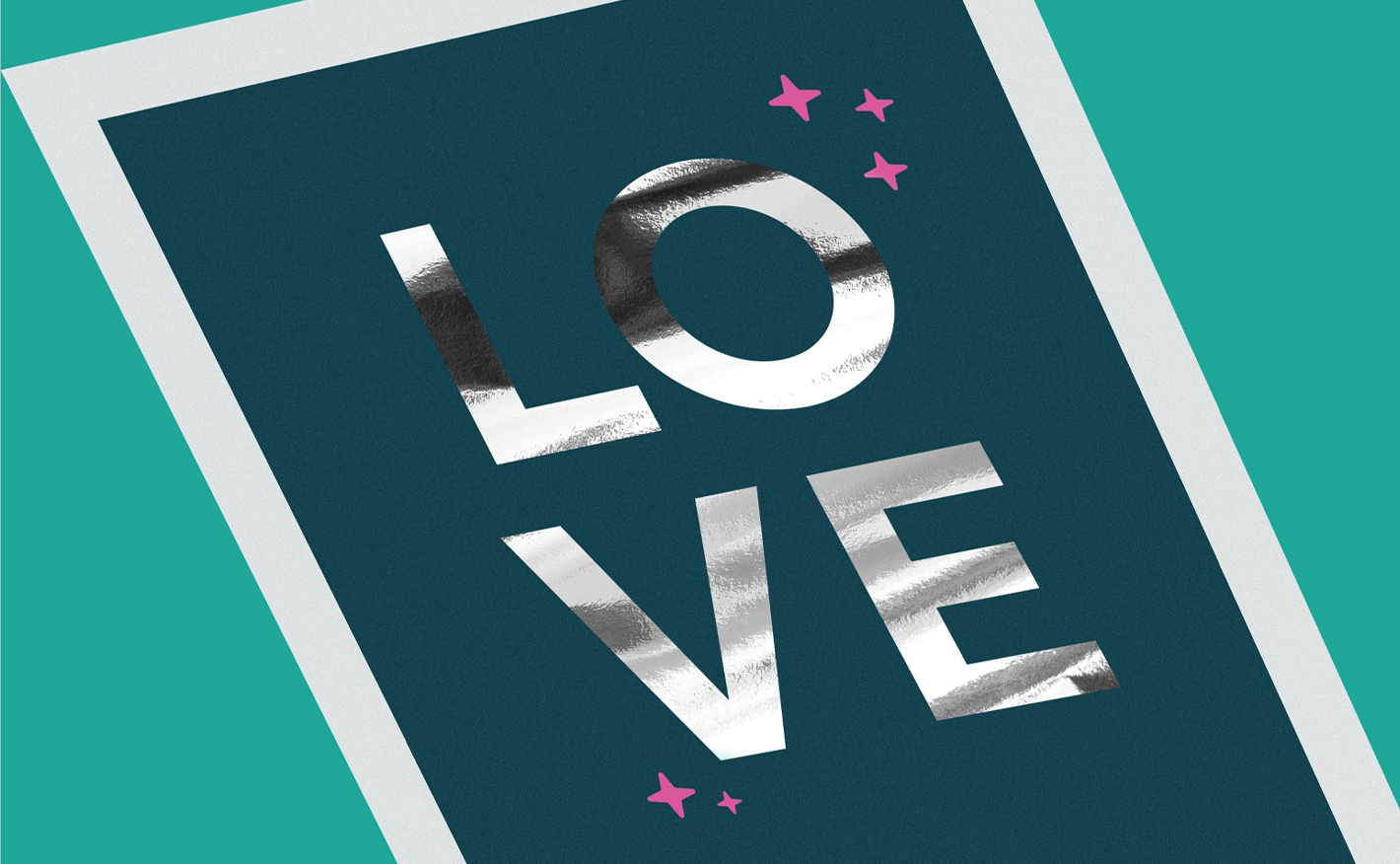 A close-up view of a dark teal card featuring the word "LOVE" in large, metallic silver foil stamping. The shiny, reflective letters are surrounded by small, pink printed star icons.