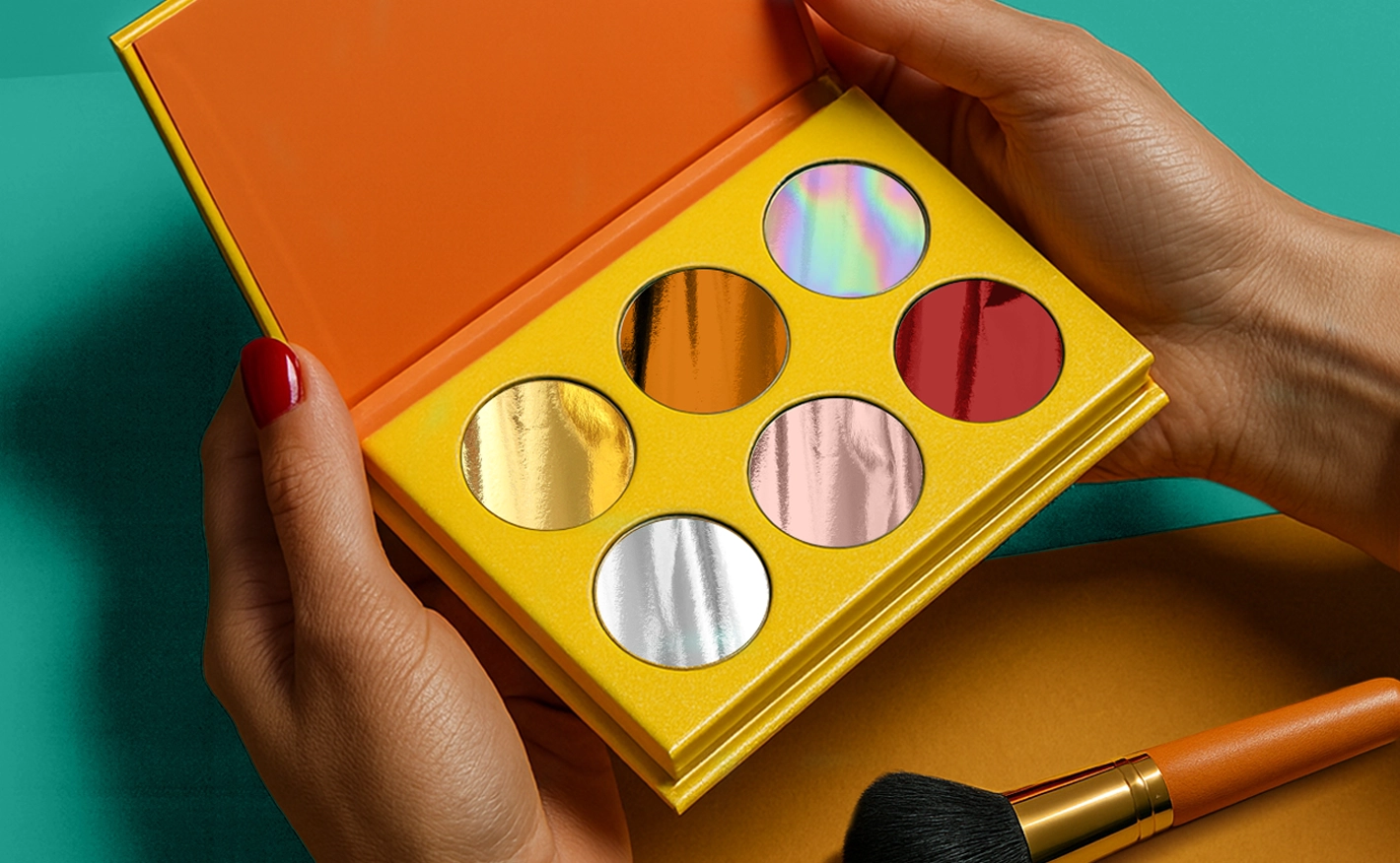 A pair of hands holds open a vibrant yellow palette showcasing six circular, metallic and holographic foil swatches against a bold teal and orange background.