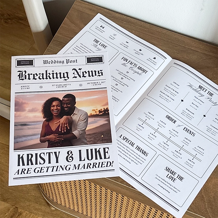 A personalized wedding newspaper titled "Wedding Post" is displayed open on a wooden table, featuring a front-page photo of a smiling couple on a beach under the headline "Kristy & Luke Are Getting Married!" alongside inner pages detailing fun facts, the wedding party, and an order of events.