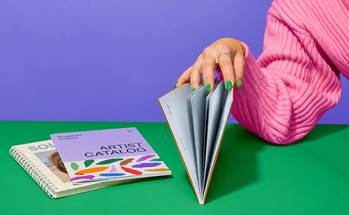 Book Binding and Printing A person fanning open a Catalog on a green surface next to other booklets.